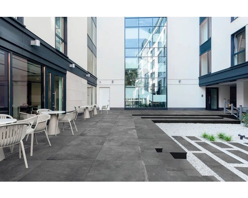 Außenbereich mit grauen Fliesen, Tischen und Stühlen vor einem modernen Gebäude.