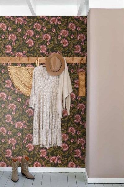 Vliestapete mit floralem Muster in Rosa und Grün in einem hellen Flur mit hölzerner Garderobe, Kleidung und Stiefeln.