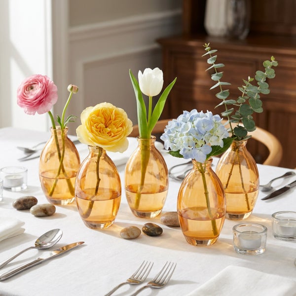 Set aus fuenf kleinen, bauchigen Glasvasen in Bernsteinoptik, dekoriert mit verschiedenen Blumen auf einem gedeckten Tisch.