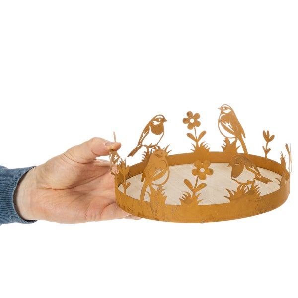 Rundes Dekotablett aus Metall mit Vogel- und Blumenmotiven in Rostoptik und Holzboden, in einer Hand gehalten.