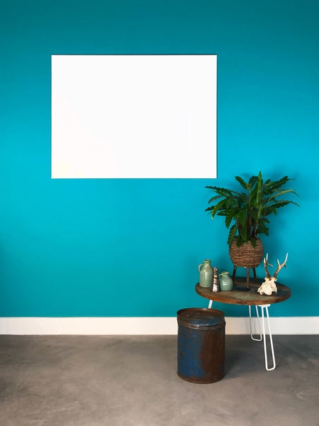 Innenraum mit türkisblauer Wand, weißem Akustikpaneel und einem Holztisch mit Pflanze. Ein rustikaler Metallbehälter steht auf dem grauen Boden.