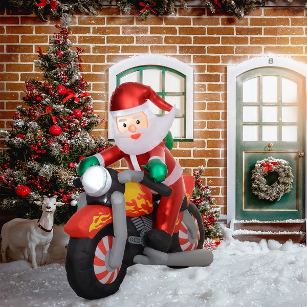 Aufblasbarer Weihnachtsmann auf einem Motorrad vor einer weihnachtlichen Kulisse mit Tannenbaum, Backsteinwand und Haustür im Schnee.
