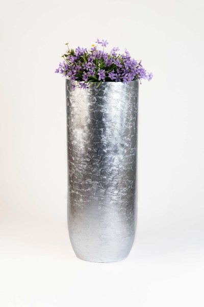 Hohe silberne Vase mit strukturierter Oberfläche und lila Blumen.