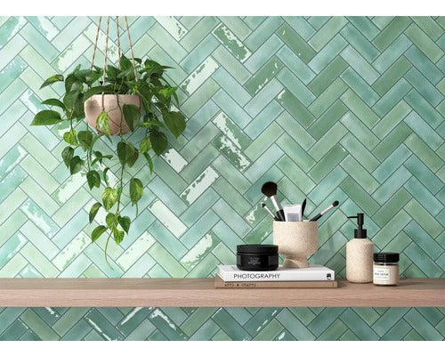 Wandgestaltung mit grünen Fliesen in Fischgrätmusteranordnung, kombiniert mit Holzregal und Dekoration
