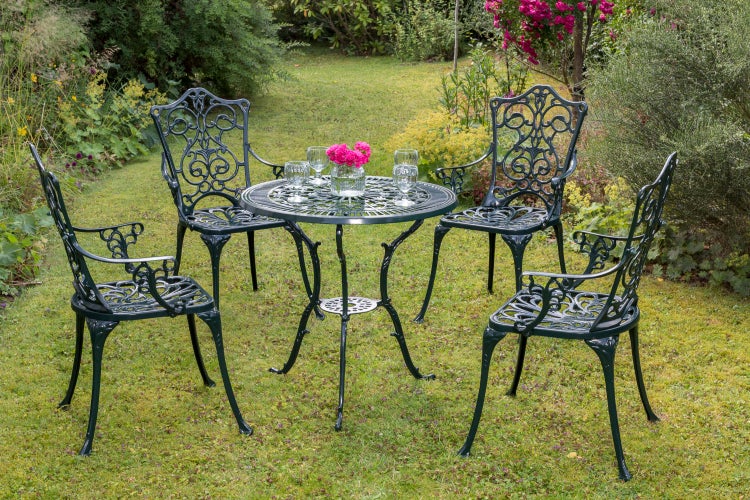 Gartenszene mit einem runden Gartentisch aus Metall mit vier passenden Stühlen, Blumenvase und Gläsern auf einer Rasenfläche