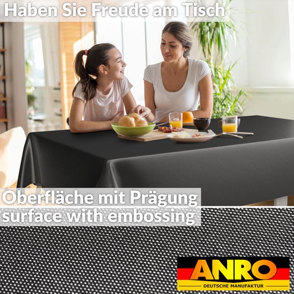 Eine Familie sitzt an einem Esstisch mit einer schwarzen Tischdecke mit geprägter Oberfläche. Detailansicht der Struktur. ANRO Logo.