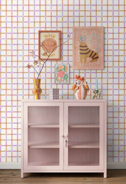 Vliestapete mit feinem farbigem Karomuster in einem hellen Zimmer über einem rosa Glasschrank mit Dekoration und Bildern.