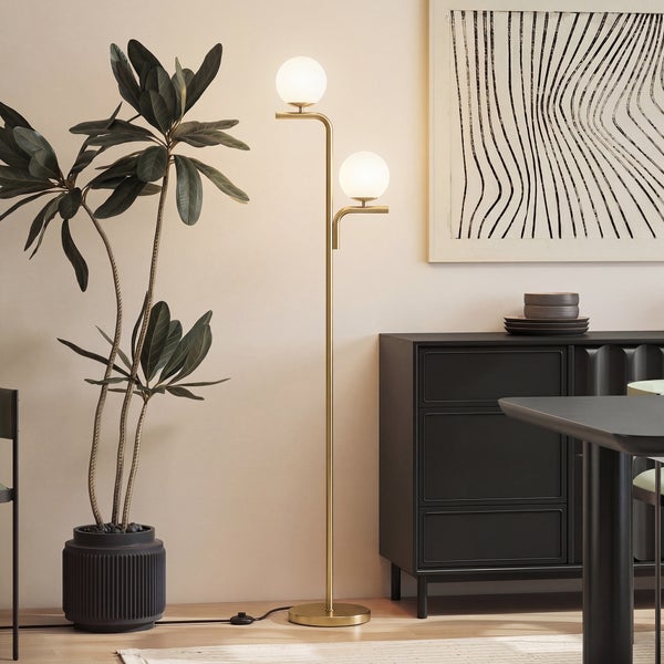 Modern eingerichtetes Zimmer mit einer zweiflammigen Stehleuchte aus Metall mit kugelförmigen Glasschirmen neben einer Zimmerpflanze.