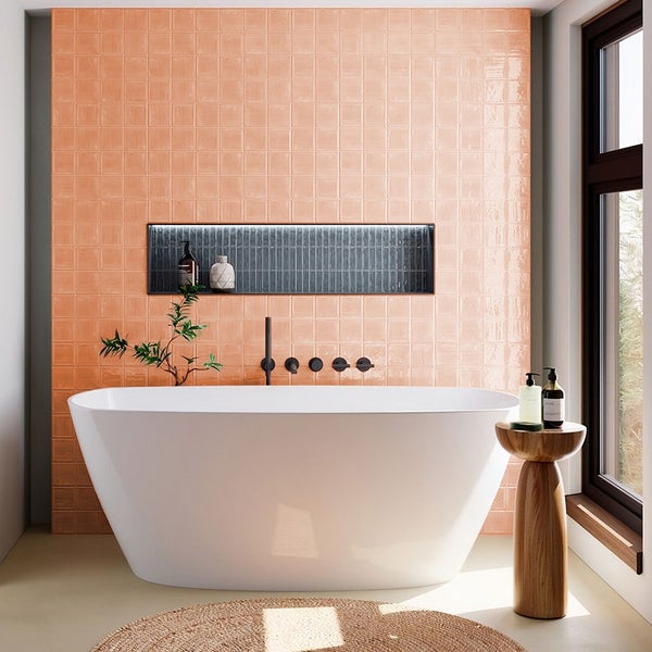 Badezimmer mit freistehender Badewanne vor einer Wand aus quadratischen Fliesen und einer integrierten Wandnische mit Armatur.