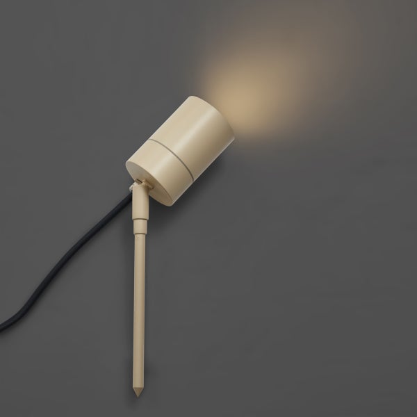 Beige Gartenstrahler mit Erdspieß und schwarzem Kabel, eingeschaltet mit warmweißem Lichtkegel.