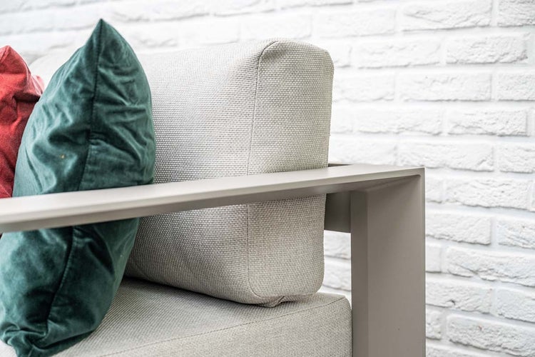 Detailaufnahme eines Garten-Loungesessels mit Metallgestell, strukturierten Polstern und Dekokissen vor einer Ziegelwand.