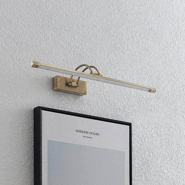 LED-Bilderleuchte aus Metall in Messing-Optik, über einem gerahmten Bild an der Wand montiert.