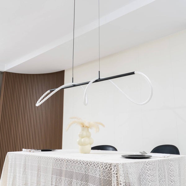 Moderne LED-Pendelleuchte mit schwarzem Metallstab und weißem Lichtelement über einem Esstisch mit Spitzentischdecke in einem hellen Esszimmer.