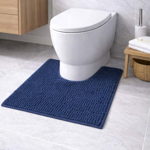 Blaue Toilettenvorlage mit Noppenstruktur vor einer weißen Toilette in einem hellen Badezimmer mit grauen Fliesen.