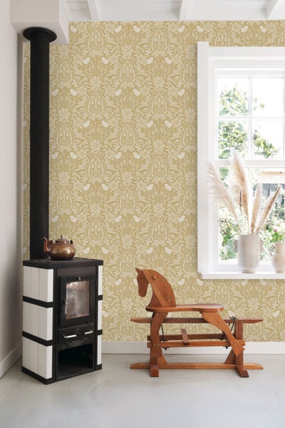 Vliestapete mit Blumen- und Vogelmuster in einem hellen Zimmer mit Kaminofen, Fenster und einem Schaukelpferd aus Holz.
