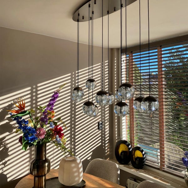 Szene mit Pendelleuchte mit mehreren Kugel Lampenschirmen über einem Esstisch mit Blumenarrangement.