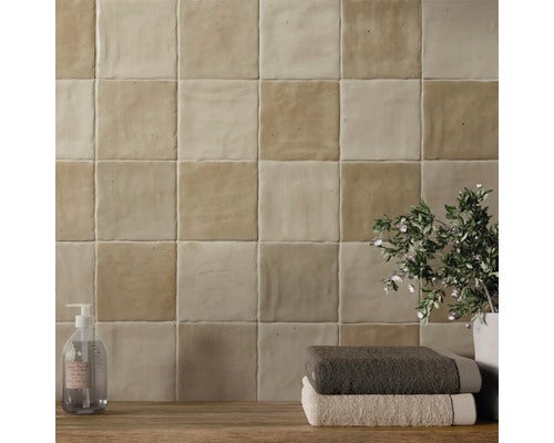 Quadratische Wandfliesen aus Keramik in Beige mit strukturierter Oberfläche im Schachbrettmuster, dekoriert mit Badaccessoires und Handtüchern.