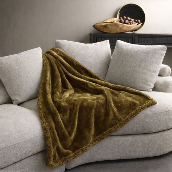 Eine weiche Wohndecke auf einem hellen Sofa mit Kissen in einem stilvoll eingerichteten Wohnzimmer.