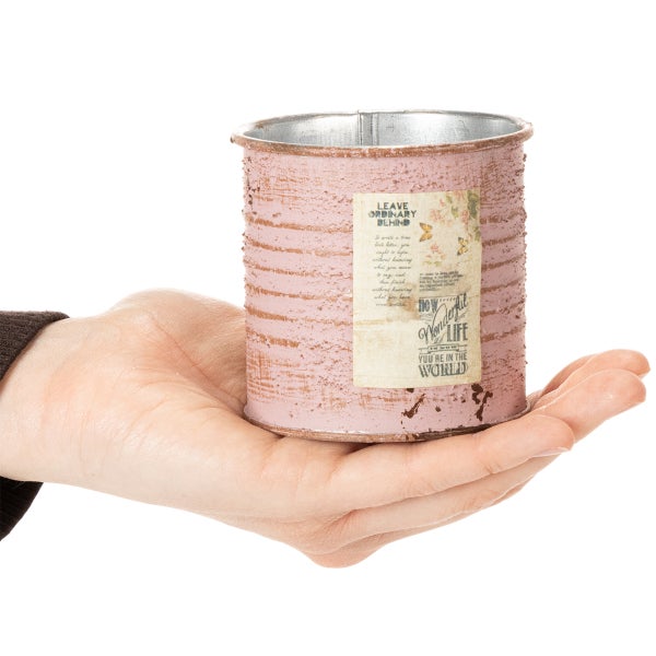Kleiner dekorativer Übertopf aus Metall im Vintage Stil, rosa strukturiert, mit einem Papieretikett mit Aufschrift, in einer Hand gehalten.