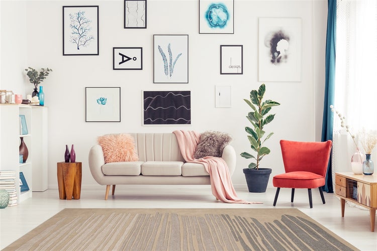Modernes Wohnzimmer mit hellem Sofa, Sessel und einer Bilderwand mit zahlreichen gerahmten Kunstdrucken über einem modernen Teppich.