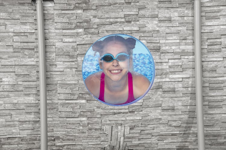 Aufstellpool in Steinoptik mit rundem Sichtfenster, durch das ein lächelndes Mädchen unter Wasser mit Schwimmbrille zu sehen ist.