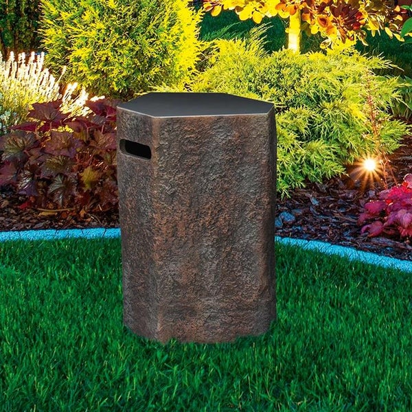 Sechseckige Gartensteckdose in Steinoptik auf einer Rasenfläche vor einem hellen Gartenbeet mit Sträuchern.