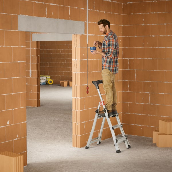 Mann auf einer Trittleiter in einem Rohbau mit Ziegelwänden