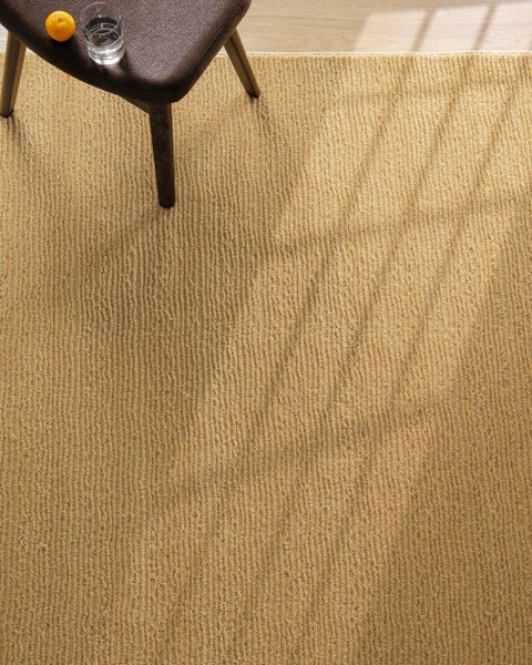 Beige Teppich mit gerippter Struktur, kombiniert mit einem dunklen Hocker in einem hellen Raum.