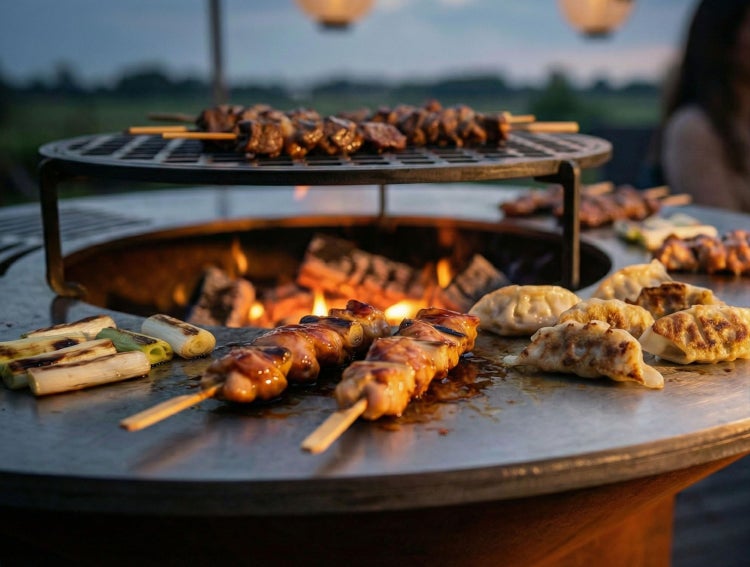 Fleischspieße, Teigtaschen und Lauch auf einer runden Feuerschale mit Grillring und erhöhtem Grillrost im Freien.