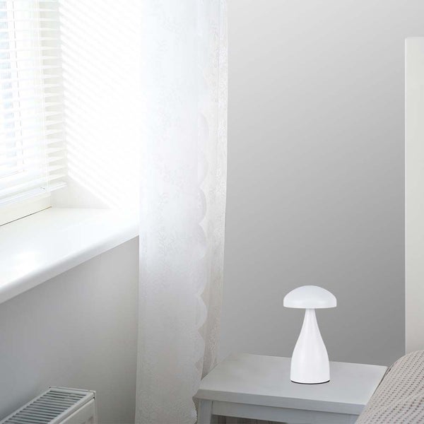 Weiße Tischleuchte auf einem Nachttisch in einem hellen Raum.