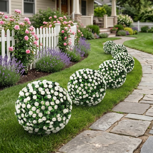 Dekorative künstliche Blumenkugeln mit weißen Rosen in einem gepflegten Garten neben einem Steinweg und einem weißen Lattenzaun.