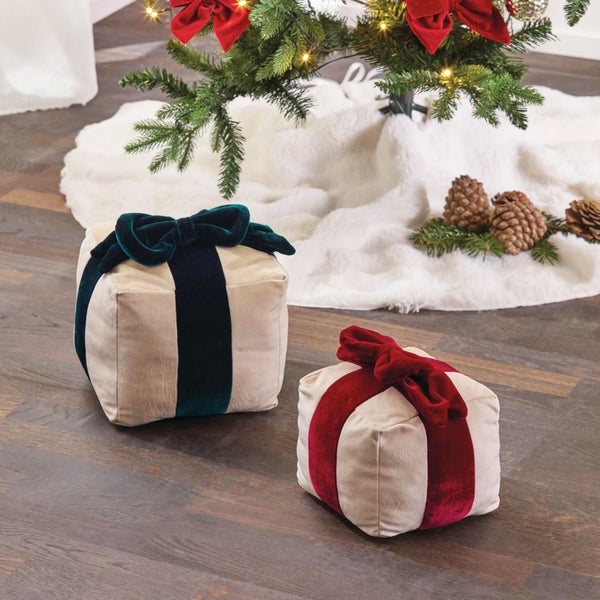 Zwei quadratische Stoffkissen in Geschenkform mit Samtschleife unter einem geschmückten Weihnachtsbaum.