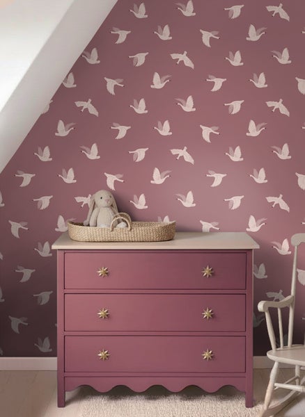 Kinderzimmer mit Tapete mit Schwanenmuster, einer rosa Kommode mit Sterngriffen und einem Plüschhasen in einem Korb.