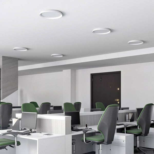 Moderne Büroumgebung mit runden flachen LED-Deckenleuchten über Arbeitsplätzen mit Schreibtischen und ergonomischen Bürostühlen.