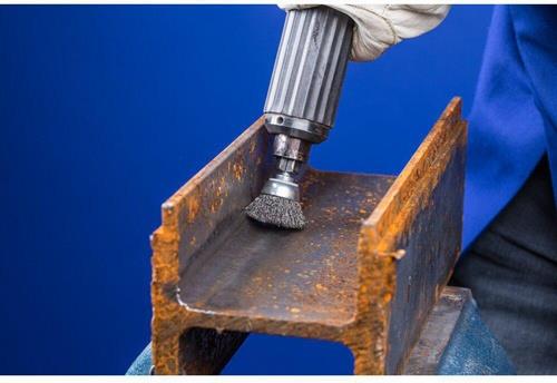 Ein Mann schleift Rost von einem Stahlträger mit einer Drahtbürste.