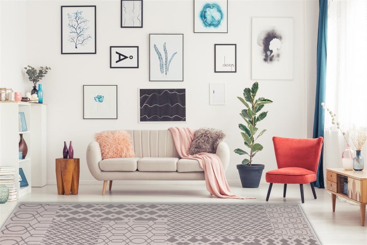 Wohnzimmer mit beigefarbenem Sofa, Sessel und modernem Teppich mit geometrischem Muster auf einer hellen Wand mit Galeriebildern.
