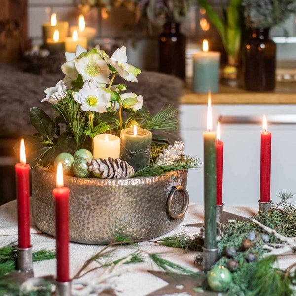 Festliche Tischdekoration mit Blumen, Kerzen und Tannenzapfen in einer Metallschale