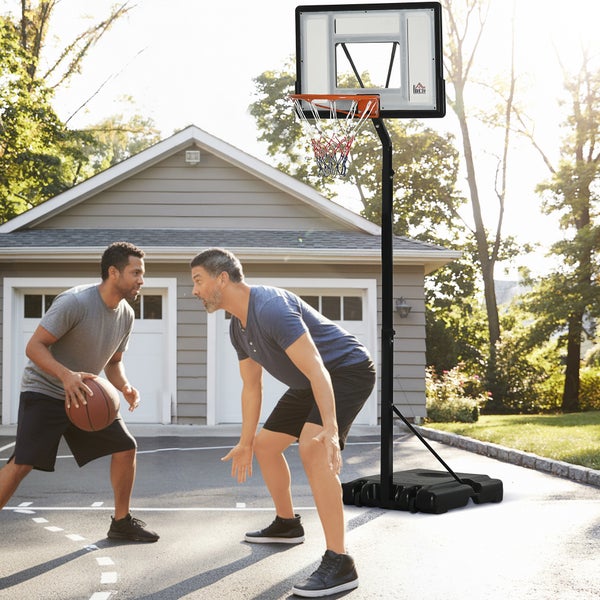 Mobiler, höhenverstellbarer Basketballkorb auf einer Einfahrt mit zwei Spielern. Schwarzer Metallständer, transparentes Backboard, befüllbarer Fuß.