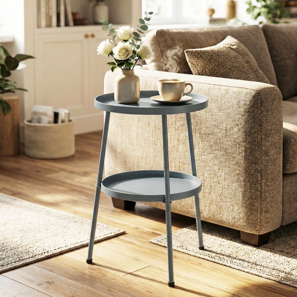 Runder Beistelltisch mit zwei Ebenen aus Metall in einem hellen Wohnzimmer neben einem beigen Sofa.