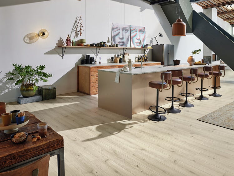 Moderne Küche in offener Bauweise mit heller Holzoptik Bodenbelag, Kücheninsel und Barhockern in einem lichtdurchfluteten Wohnbereich.