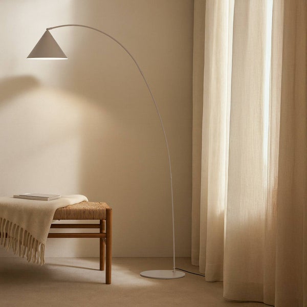 Bogenlampe neben Bank mit Decke und Buch in einem hellen Raum.