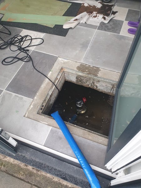 Moderne LED-Pendelleuchte in Schiffchenform, außen schwarz und innen goldfarben, über einem Holztisch mit einer kleinen Pflanze.