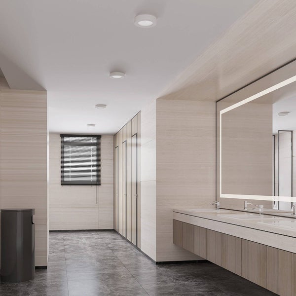 Modernes helles Badezimmer mit runden LED-Deckenleuchten, großem beleuchtetem Spiegel, schwebendem Waschtisch und dunklem Steinboden.