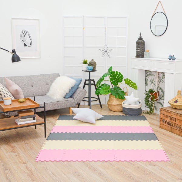 Gestreifte Puzzlematte aus Schaumstoff in einem hellen Wohnzimmer mit grauem Sofa, Pflanzen und Holzfußboden.