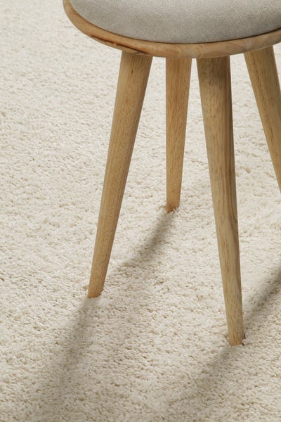 Hocker mit Holzbeinen und gepolsterter Sitzfläche auf einem Hochflor-Teppich.