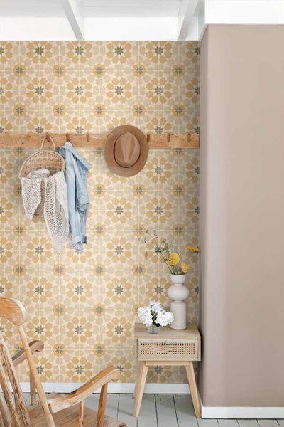 Helles Zimmer mit geometrisch gemusterter Wand. Eine hölzerne Hakenleiste mit Korb und Hut sowie ein kleiner Beistelltisch ergänzen den Raum.