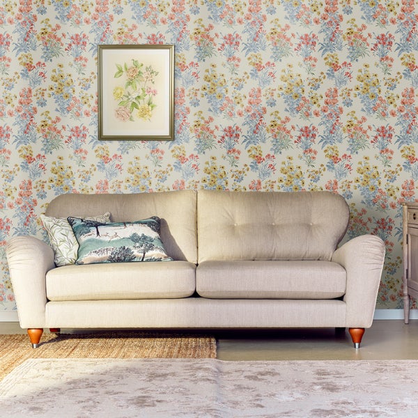 Beigefarbenes Sofa vor einer Wand mit Blumenmuster Tapete und einem gerahmten Bild