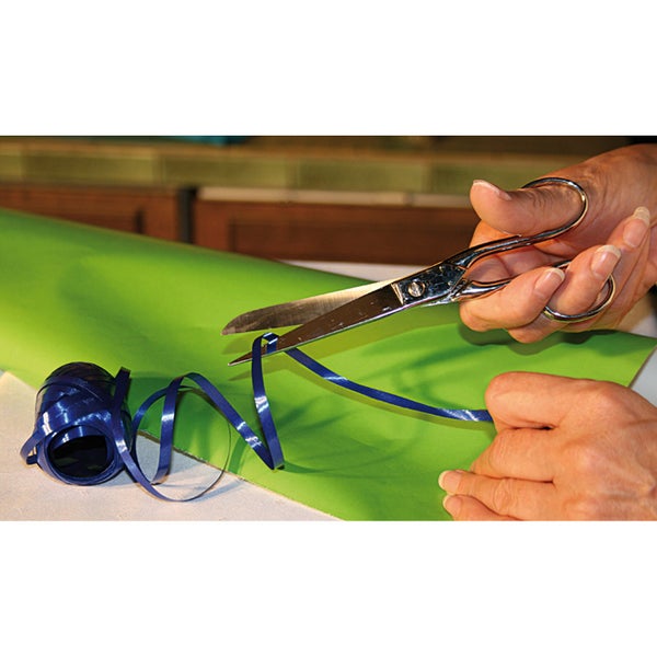 Hände benutzen eine Metallschere, um ein blaues Geschenkband auf grünem Geschenkpapier zu kräuseln.