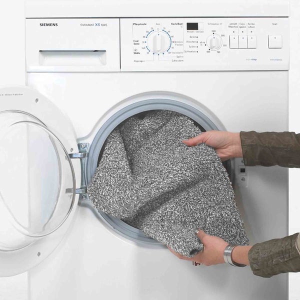 Person legt grauen Teppich in eine weiße Siemens Waschmaschine
