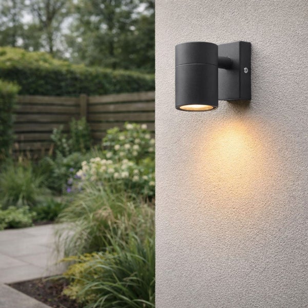 Moderne zylindrische Außenwandleuchte an einer strukturierten Hauswand im Garten, Lichtstrahl nach unten gerichtet.